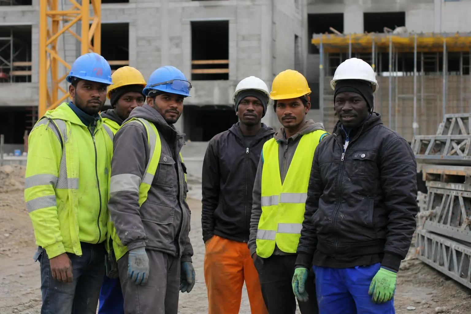 Groupe de travailleurs du BTP sur un chantier, portant casques et gilets réfléchissants, debout devant une construction en cours. coÃ»t main-d'œuvre btp étrangère.