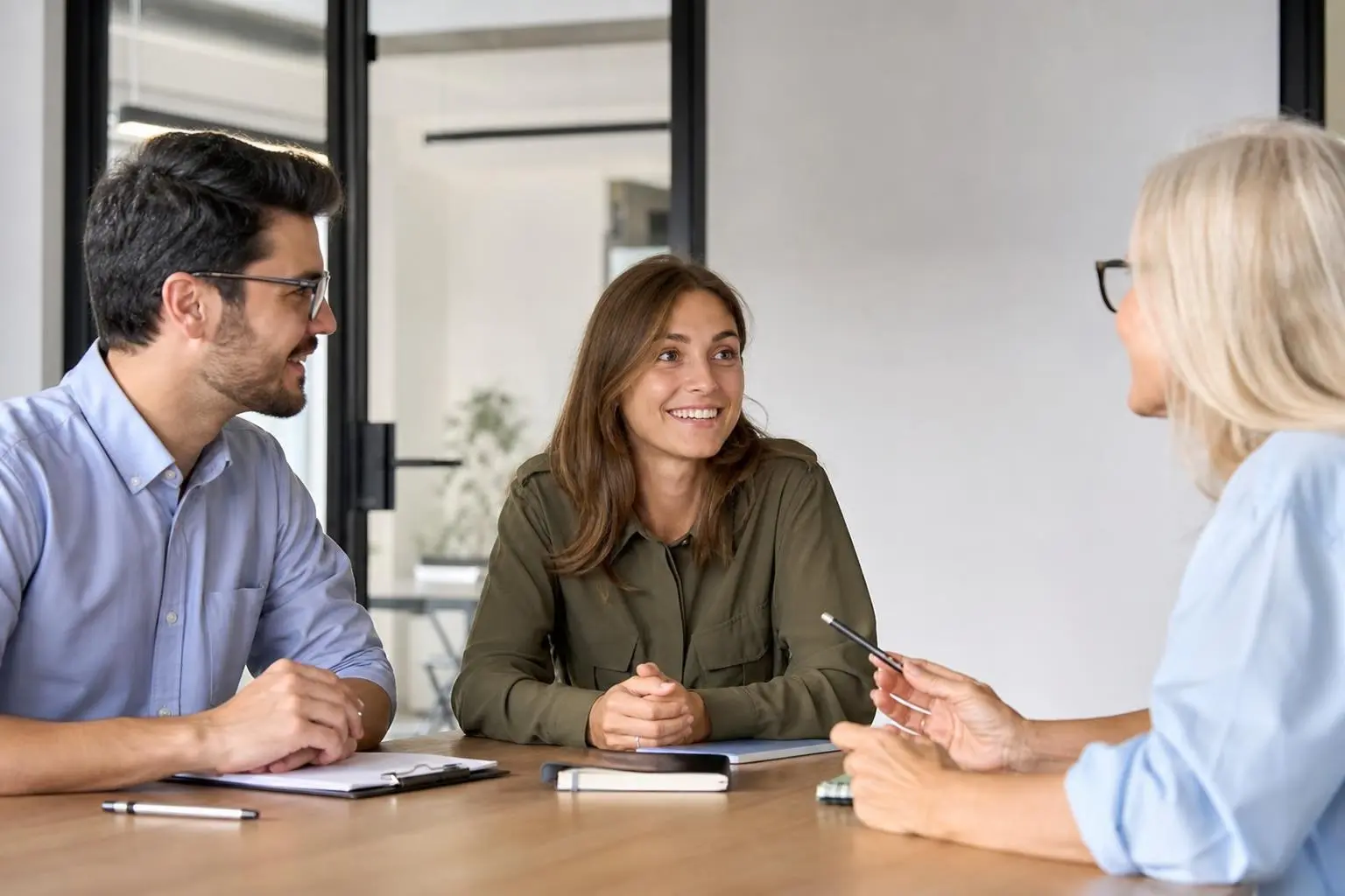 Trois personnes en entretien: une femme souriante au centre écoute, discutent et prennent des notes, exprimant un processus recrutement intérim rapide.
