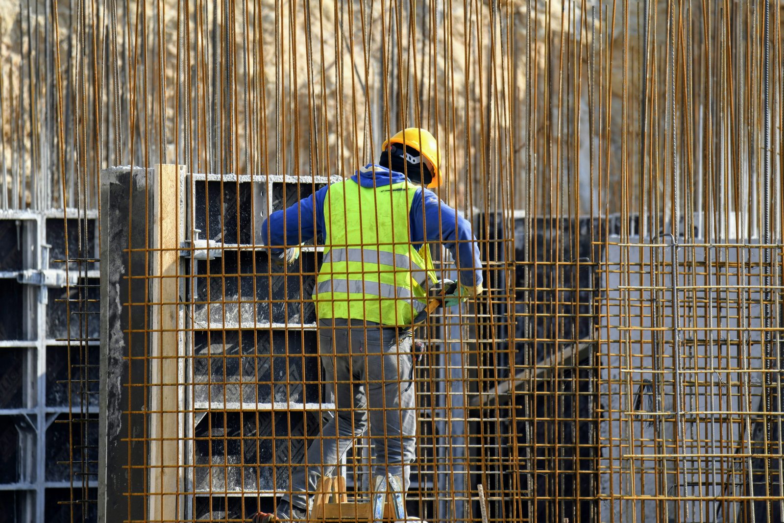 Ouvrier sur un chantier, casque jaune et gilet réfléchissant, travaillant parmi une structure en acier à treillis. 4 niveaux de qualification dans le bâtiment mentionné.
