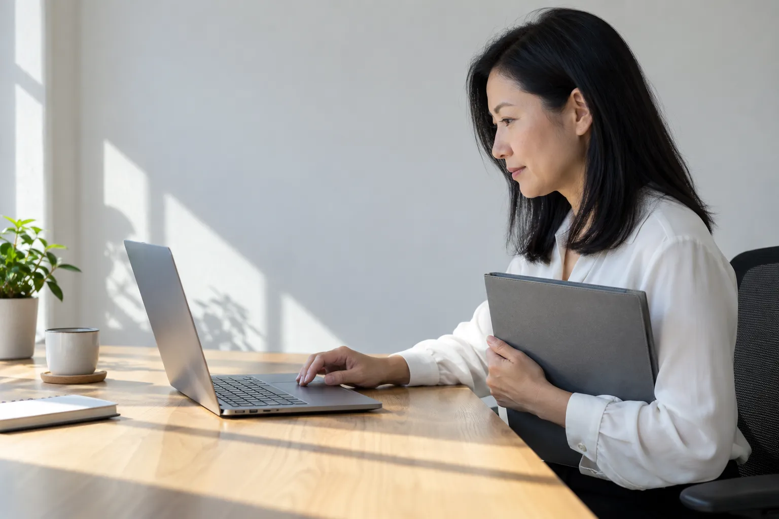 Une femme assise à un bureau travaille sur un ordinateur portable et tient un dossier près d’elle.